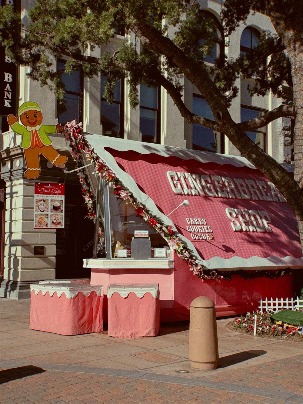 The Gingerbread Shop's pink A-frame booth on Mission Inn Avenue, with our gingerbread man in a green jacket waving above the Festival of Lights menu sign
